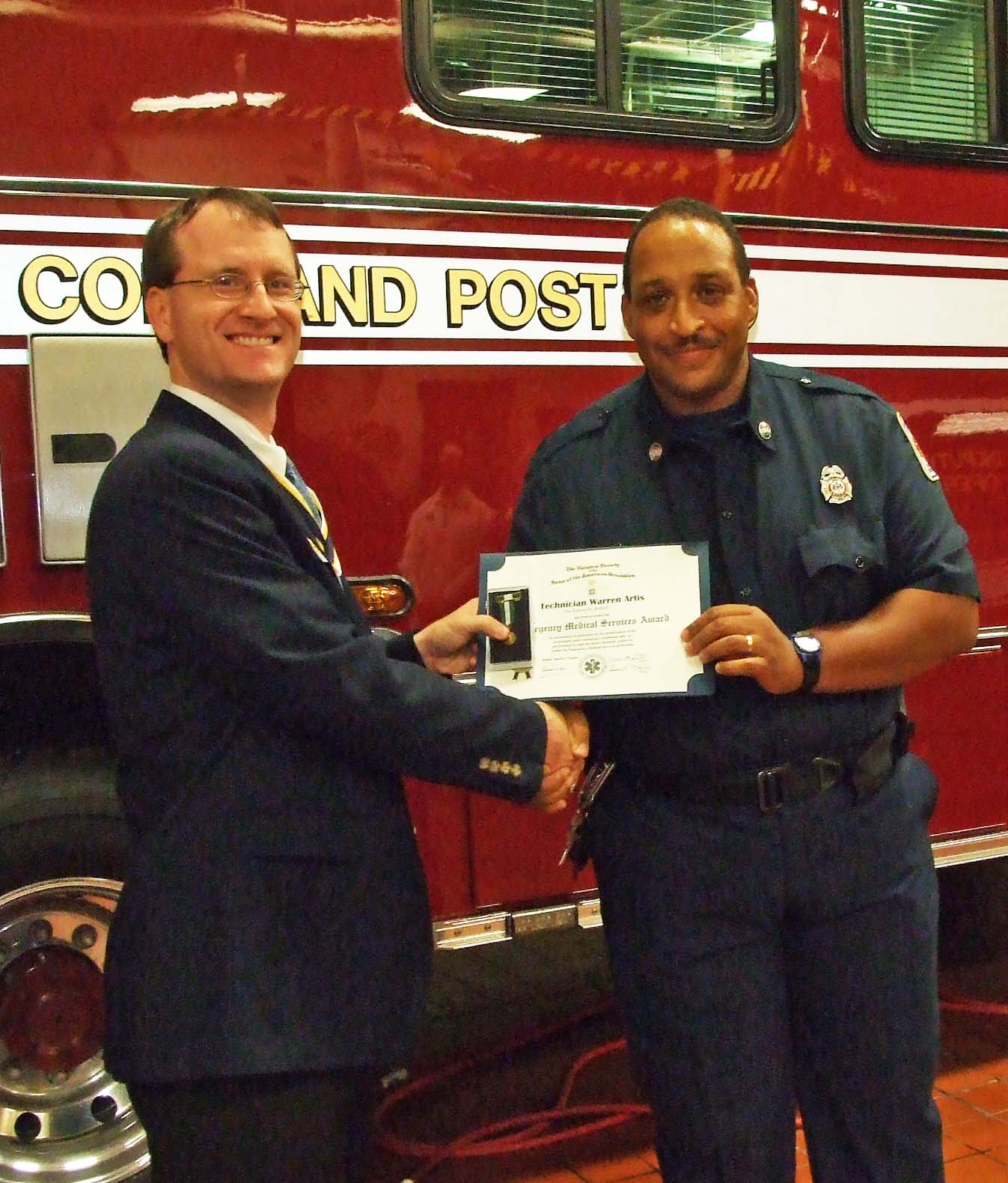 Warrn Artis receives the Fairfax Resolves EMS Commendation from Chapter President Darrin Schmidt. The station's mobile command post vehicle serves as a backdrop.